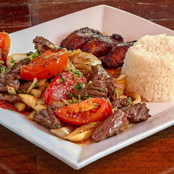 Cuban dish with beef, tomatoes, onions, fried plantains, and white rice on a white plate.