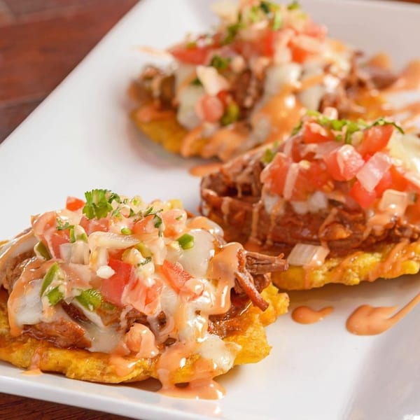 Three Cuban tostones topped with shredded beef, melted cheese, diced tomatoes, onions, and sauce.