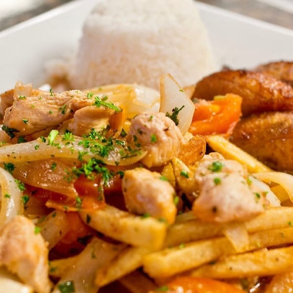Cuban chicken dish with onions, tomatoes, french fries, and a side of white rice.